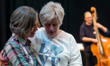 Two white women dancing together with a white male cellist in the background