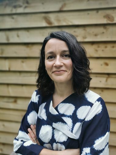 White female with dark hair wearing patterned top. Half-body portrait photo.