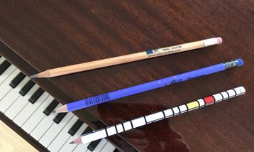 Three pencils on top of a piano viewed from above.