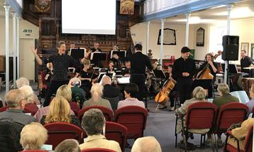 An audience watching a performance by a small orchestra and two singers.