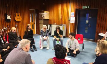 Musicians and young people sat in a circle in a workshop