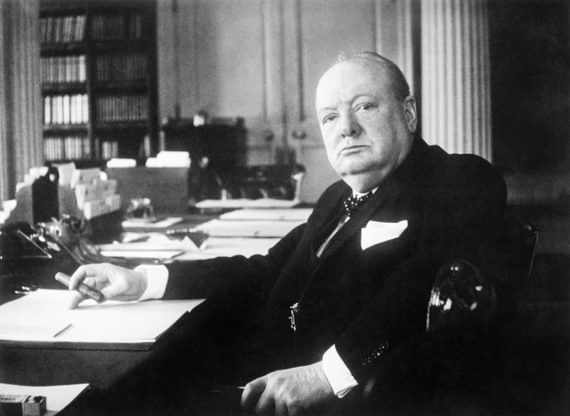 Sir Winston Churchill sits in an office looking at the camera