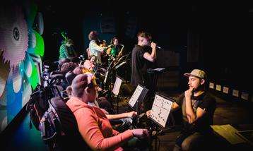 Young musicians performing using wheelchair controllers, a beatboxer on stage in front of them.
