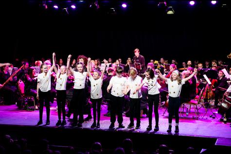 Group of students on stage with hands raised