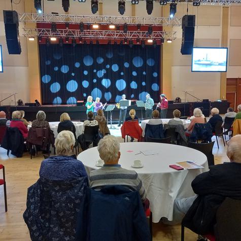 Audience seated on round tables watching an orchestra perfom