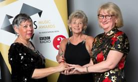 Three women holding an award in front of a banner