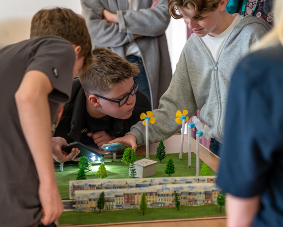 Group of children looking at wind turbine models, one blows into it