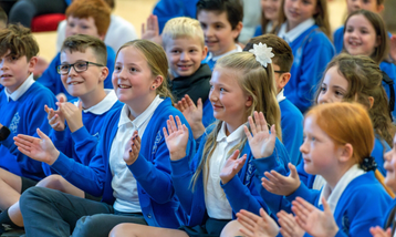 Group of school students seated with hands raised and smiling