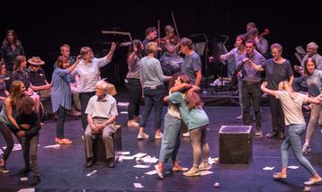 Performers acting on stage, two women at the front embracing.