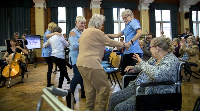 Care home staff and residents dancing in front of an orchestra.
