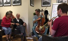 An elderly man conducting two musicians playing cello and trumpet.