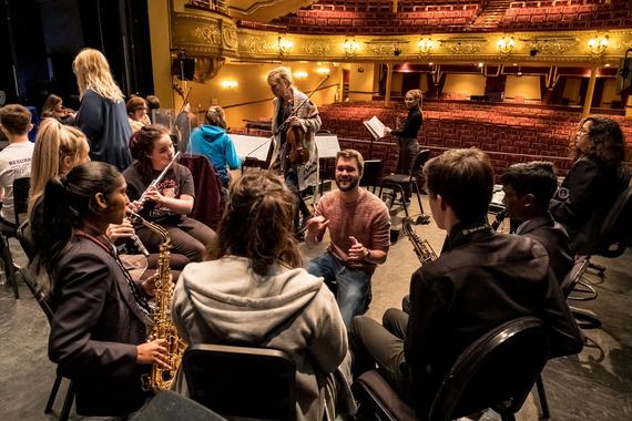 A music leader conducting a semi circle of young musicians in rehearsal.