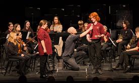 Music leader holds microphone to young student on stage