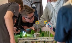 A young boy blows on a miniature wind turbine model
