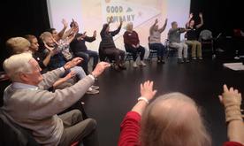 Large group of people with hands raised with a Good Company projection behind them