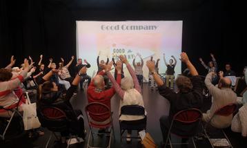 Group of people with hands raised, a good company projection behind them