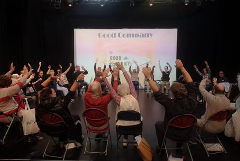 Group of people with hands raised, a good company projection behind them