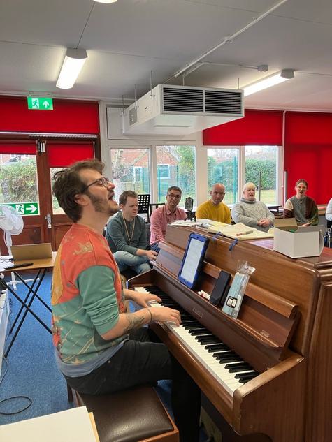 A man playing a piano singing with a group of people