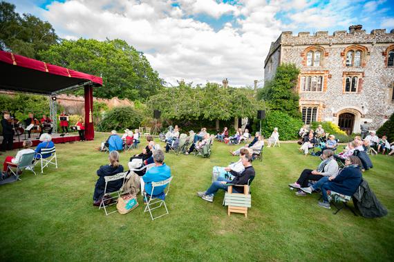 A large lawn with musicians on stage and audience seating spread across