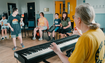 Young boy in music workshop stands, man plays piano as the boy dances