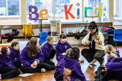 Primary school students seated listening to a musician
