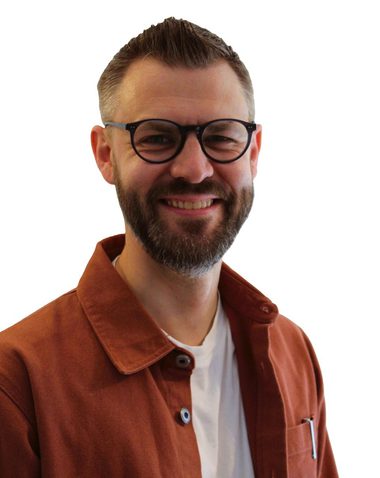 Headshot of Giles Wright, Chair of Orchestras Live, wearing a white t-shirt and orange over shirt. He is white and has a beard, glasses and short brown hair