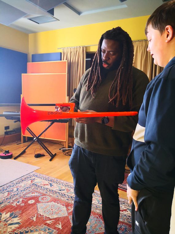 Music instructor demonstrating a bright red trombone to a student in a rehearsal studio.