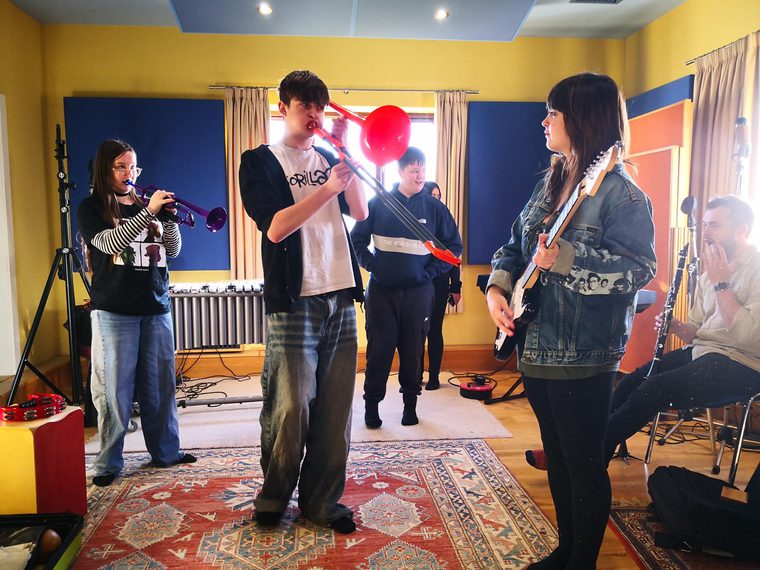 Group of young musicians rehearsing in a studio, playing trumpet, trombone, electric guitar, and clarinet.